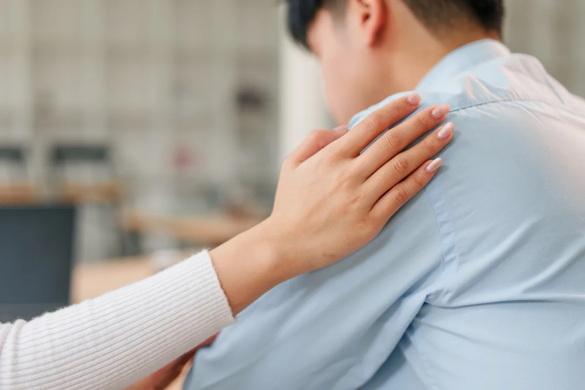Two people seated together, one offering a supportive hand